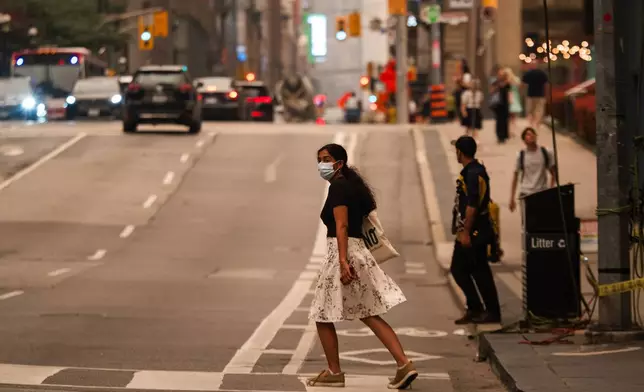 A woman wearing a mask crosses the street in Toronto as wildfire smoke fills the city, on Wednesday, July 15, 2026. (Laura Proctor/The Canadian Press via AP)