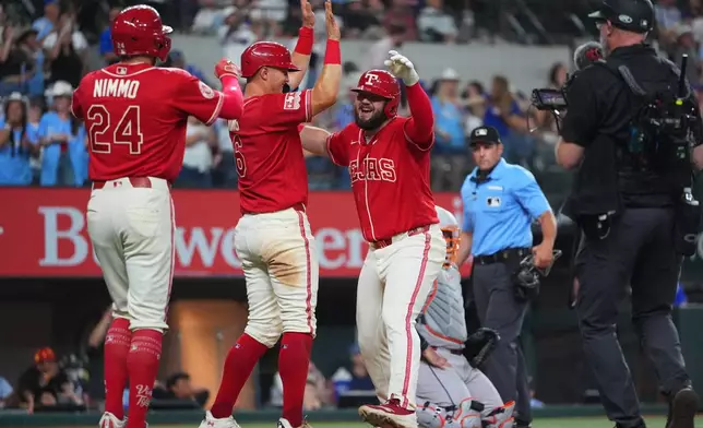 Texas Rangers Jake Burger, right, celebrates his home run scoring teammates Brandon Nimmo (24) and Josh Jung during the 8th inning of a baseball game against the Houston Astros, Friday, July 10, 2026, in Arlington, Texas. (AP Photo/LM Otero)