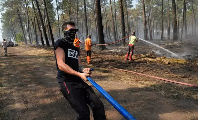 Local residents hose down smoldering fires in a forest in Souge, during wildfires in southwestern France, Wednesday, July 29, 2026. (AP Photo/Baz Ratner)
