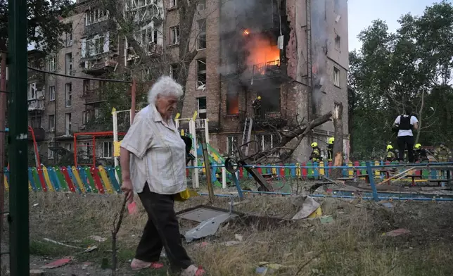 A woman walks past a burning apartment building after a Russian missile attack in Kyiv, Ukraine, Thursday, July 2, 2026. (AP Photo/Danylo Antoniuk)