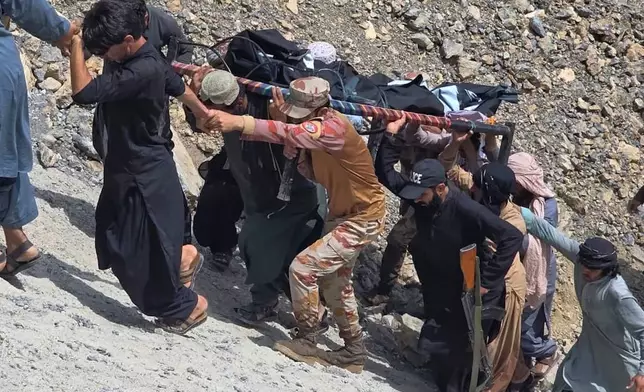 Soldiers and volunteers transport a body after recovering him as an overcrowded passenger bus plunged from a highway into a rocky ravine, in Dana Sar, a remote area near the border of Balochistan and Khyber Pakhtunkhwa provinces, in southwestern Pakistan, Friday, July 3, 2026. (AP Photo/Zain Ullah)