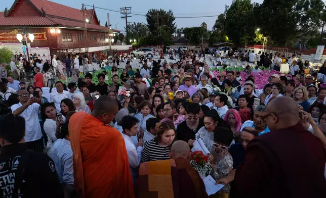 Bhikkhu Pannakara, bottom center, a Buddhist monk who led a Walk for Peace from Fort Worth, Texas, to Washington, D.C., hands out postcards and signs autographs for attendees at Wat Thai of Los Angeles in the North Hollywood section of Los Angeles, Monday, July 13, 2026. (AP Photo/Jae C. Hong)