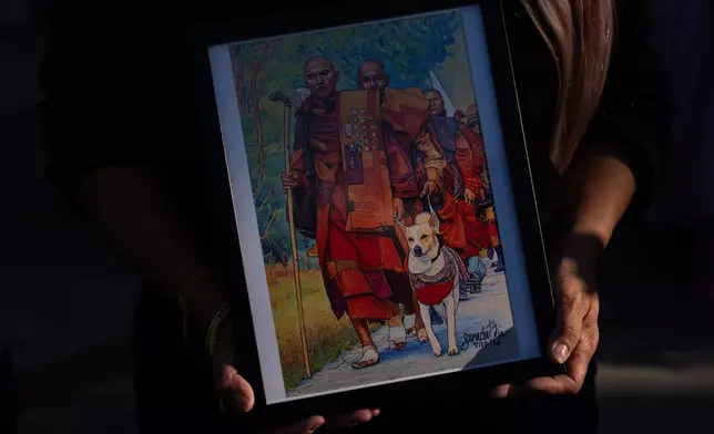 An attendee holds a framed painting depicting Bhikkhu Pannakara, a Buddhist monk who led a Walk for Peace from Fort Worth, Texas, to Washington, D.C., and his dog, Aloka, during an event at Wat Thai of Los Angeles in the North Hollywood section of Los Angeles, Monday, July 13, 2026. (AP Photo/Jae C. Hong)