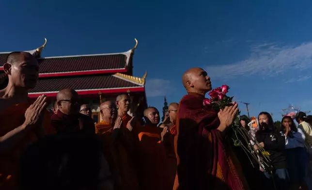 Bhikkhu Pannakara, foreground right, a Buddhist monk who led a Walk for Peace from Fort Worth, Texas, to Washington, D.C., carries flowers as he pays his respects at a monument during an event at Wat Thai of Los Angeles in the North Hollywood section of Los Angeles, Monday, July 13, 2026. (AP Photo/Jae C. Hong)
