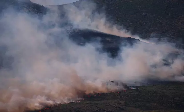A firefighting helicopter drops water on the flames as a wildfire advances near Burgohondo, Ávila province, Spain, Friday, July 24, 2026. (AP Photo/Manu Fernandez)