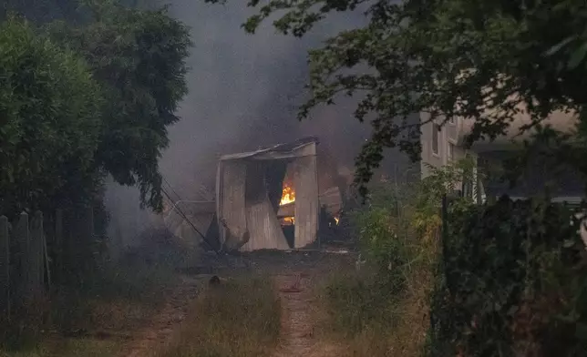 A burning barn is seen next to a farm house during wildfires near Le Porge, western France, Thursday, July 23, 2026. (AP Photo/Caroline Blumberg)