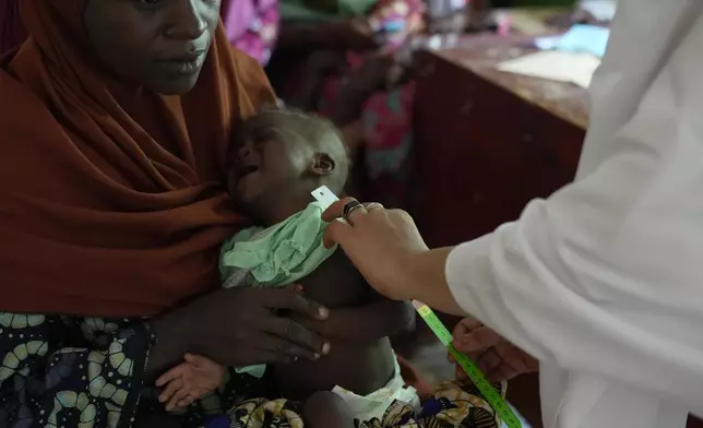 Halimah Muhammad, a local health worker, right, attends to a child suffering from malnutrition, as his mother Larai Malami, a 35-year-old mother of 10, holds him at the Rumbukawa Primary Health Centre in Sokoto, northwestern Nigeria, Thursday, July 16, 2026. (AP Photo/Sunday Alamba)