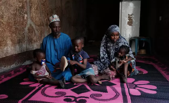 Shehu Aminu, second left, who lost his job as a taxi driver due to a spike in the retail price of petrol in February, sits with his wife Maryam Aminu, their daughter Farisa, left, who has relapsed into malnutrition, and her siblings, at their house in Kware Sokoto, northwestern Nigeria, Wednesday, July 15, 2026. (AP Photo/Sunday Alamba)