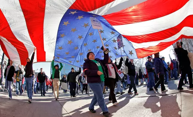 FILE - AFSCME member Merryann Wen helps hold up an American flag as she marches around the Capitol Square in Madison, Wis., Feb. 19, 2011. (AP Photo/Andy Manis, File)