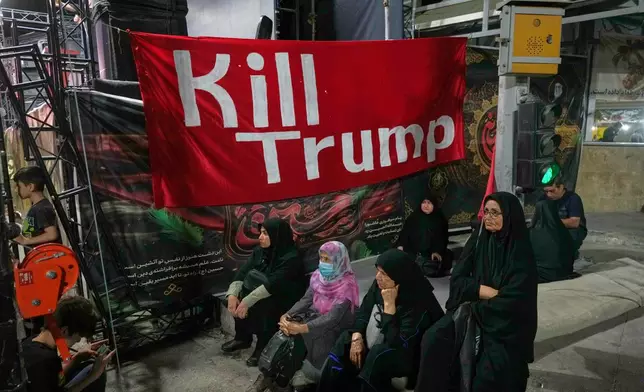 Women sit beneath a banner reading in English, "Kill Trump," during a pro-government rally in Tehran, Friday, July 17, 2026. (AP Photo/Vahid Salemi)