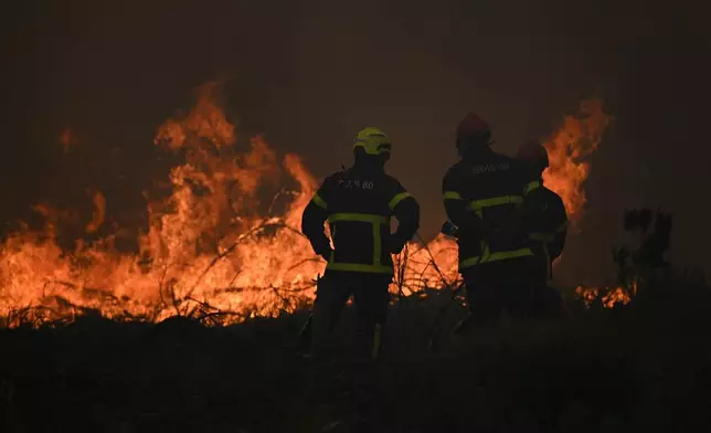 Firefighters spray water in a burning forest near Lacanau, southwestern France, Saturday, July 25, 2026. (AP Photo/Emma Da Silva)