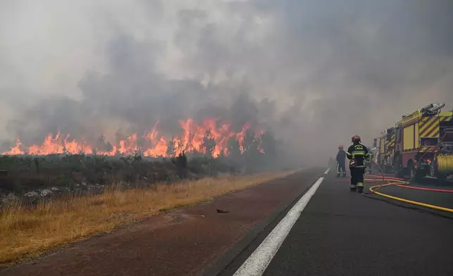 Firefighters spray water in a burning forest near Lacanau, southwestern France, Saturday, July 25, 2026. (AP Photo/Emma Da Silva)