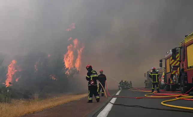 Firefighters spray water in a burning forest near Lacanau, southwestern France, Saturday, July 25, 2026. (AP Photo/Emma Da Silva)