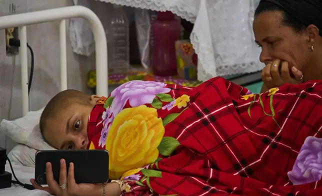 Salet Fernandez, a 17-year-old oncology patient, looks at her phone as her mother Yarima Mesa sits by her bed at the National Institute of Oncology and Radiobiology in Havana, Cuba, Wednesday, June 24, 2026. (AP Photo/Ramon Espinosa)