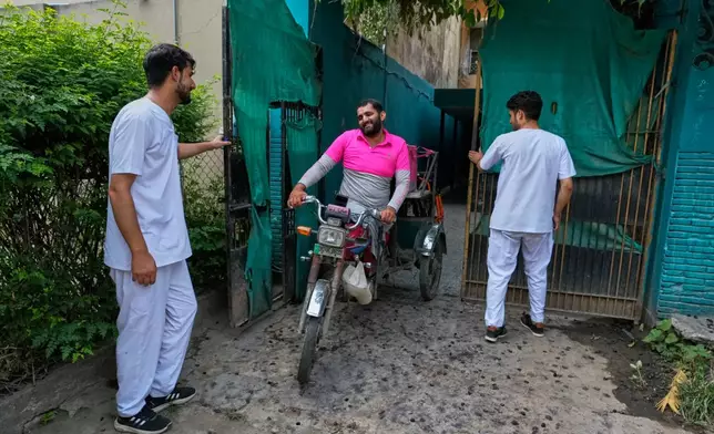 Hamza Ali, 28, who lost both legs in a road accident, leaves for work, with his roommates helping him with the gate in Islamabad, Pakistan, Friday, July 17, 2026. (AP Photo/Anjum Naveed)