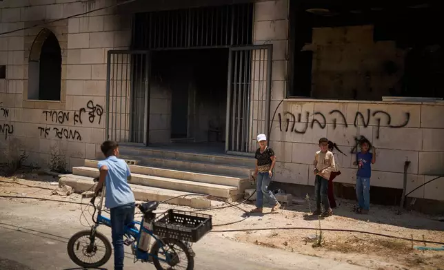 Children stand outside a mosque that was burned during an attack by Israeli settlers early in the morning in the West Bank village of Qusra, Sunday, July 26, 2026, as on its wall a Hebrew graffiti reads "Revenge Benayahu", referring to an Israeli settler killed during clashes with Palestinians in the village of Tell, last Friday. (AP Photo/Leo Correa)