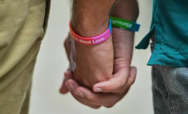 Two men hold hands at the memorial site commemorating the victims near the scene where a car rammed into a crowd near the Pride March in Berlin, Germany, Sunday, July 26, 2026. (AP Photo/Markus Schreiber)
