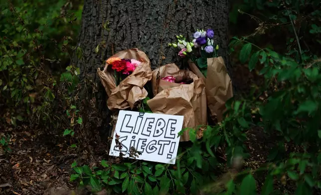 Flowers lay at a tree with a sign reading in German "Love wins", near the scene where a car rammed into a crowd in the Tiergarten Park, near the Pride March in Berlin, Germany, Sunday, July 26, 2026. (AP Photo/Markus Schreiber)