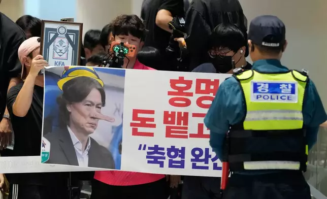 Soccer fans hold a banner showing an image of South Korea's soccer head coach Hong Myung-bo, who has resigned, as they wait for his arrival following the team's early elimination from the World Cup soccer tournament, at the Incheon International Airport in Incheon, South Korea, Tuesday, June 30, 2026. The signs read "Hong Myung-bo! Spit the money and get out! Dismantle Korea Football Association". (AP Photo/Ahn Young-joon)