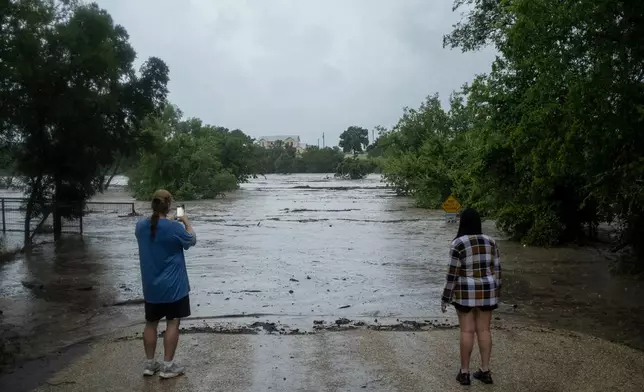 Mike Erulenfeld and Kala Martin watch as the Pedernales River floods near Old Kerr Highway on Thursday, July 16, 2026, in Fredericksburg, Texas. (AP Photo/Joel Angel Juarez)