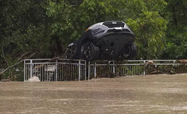 A flood-damaged car hangs from a fence on Wednesday, July 15, 2026, in Boerne, Texas. (AP Photo/Darren Abate)