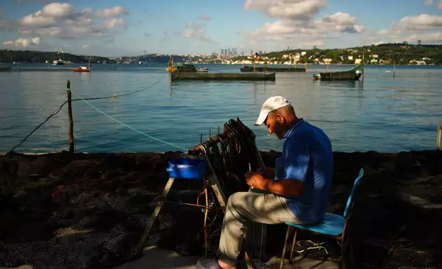 Fisherman Murat Sevilmis repairs a fishing net on the bank of the Bosphorus Strait in Istanbul, Turkey, Wednesday, June 24, 2026. (AP Photo/Emrah Gurel)