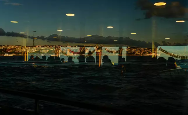 Reflected in a window, commuters cross the Bosphorus Strait in a ferry at the end of the work day in Istanbul, Turkey, Monday, July 13, 2026.(AP Photo/Emrah Gurel)