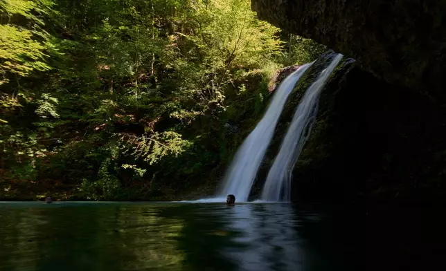 People swim beneath a waterfall in the Enipeas Gorge on Mount Olympus in northern Greece, Tuesday, July 14, 2026. (AP Photo/Petros Giannakouris)