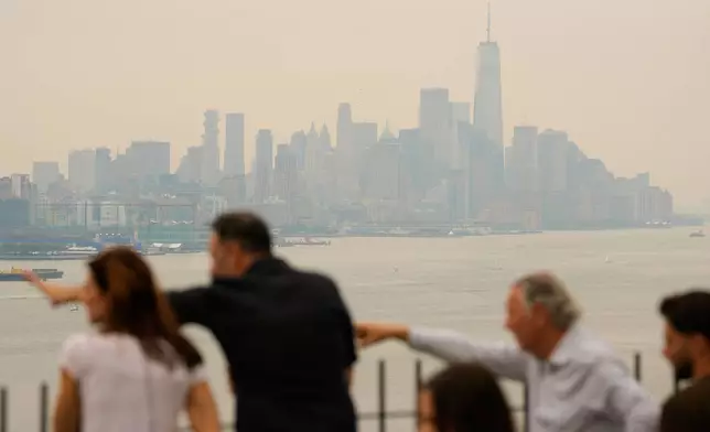 People look over the New York City skyline shrouded in smoke in Weehawken, N.J., Thursday, July 16, 2026. (AP Photo/Seth Wenig)
