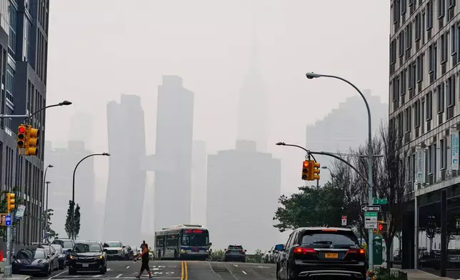 Pedestians cross Borden Avenue as the New York City skyline is obscured during poor air quality due to smoke from Canadian wildfires Thursday, July 16, 2026, in the Queens borough of New York. (AP Photo/Frank Franklin II)