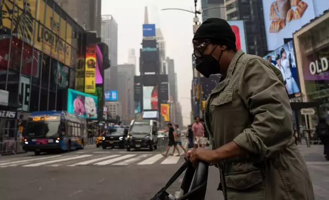 A person wearing a mask walks in Times Square as smoke from wildfires blankets the sky, Thursday, July 16, 2026, in New York. (AP Photo/Yuki Iwamura)