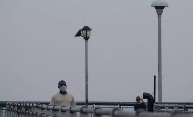 A person wearing a mask walks on a pier as smoke from wildfires blankets the sky, Thursday, July 16, 2026, in the Brooklyn borough of New York. (AP Photo/Yuki Iwamura)