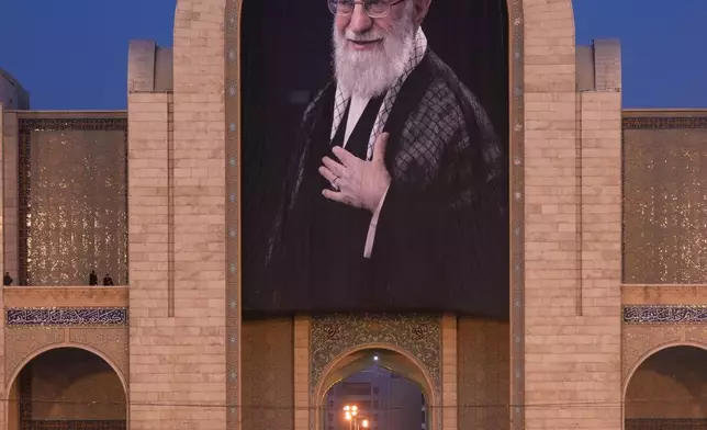 Mourners gather beneath a portrait of the late Iranian Supreme Leader Ayatollah Ali Khamenei during the funeral ceremonies for Khamenei and members of his family at the Imam Khomeini Mosalla Grand Mosque in Tehran, Iran, Saturday, July 4, 2026. (AP Photo/Altaf Qadri)