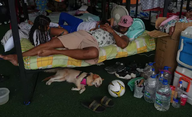 A family rests at a sports center being used as a shelter for those displaced by the earthquakes in La Guaira, Venezuela, Thursday, July 9, 2026. (AP Photo/Ariana Cubillos)