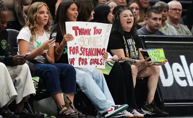 A fan holds a sign for Indiana Fever guard Sophie Cunningham in reference to her comments on transgender athletes as a fan wearing Seattle Storm gear holds a competing sign during the first half of a WNBA basketball game, Tuesday, July 28, 2026, in Seattle. (AP Photo/Lindsey Wasson)
