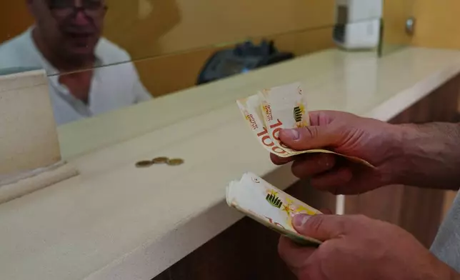 A customer counts Israeli Shekels at a currency exchange bureau in the West Bank city of Bethlehem, Tuesday, July 7, 2026. (AP Photo/Mahmoud Illean)
