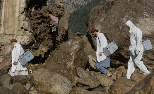 Medical workers carry equipment through an area damaged by heavy flooding in the eastern province of Nuristan, Afghanistan, Tuesday, July 21, 2026. (AP Photo/Wahidullah Kakar)