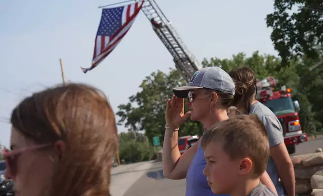 A woman salutes during a procession for firefighters who died battling wildfires near the Colorado-Utah border in Grand Junction, Colo., Monday, June 29, 2026. (AP Photo/Ty ONeil)