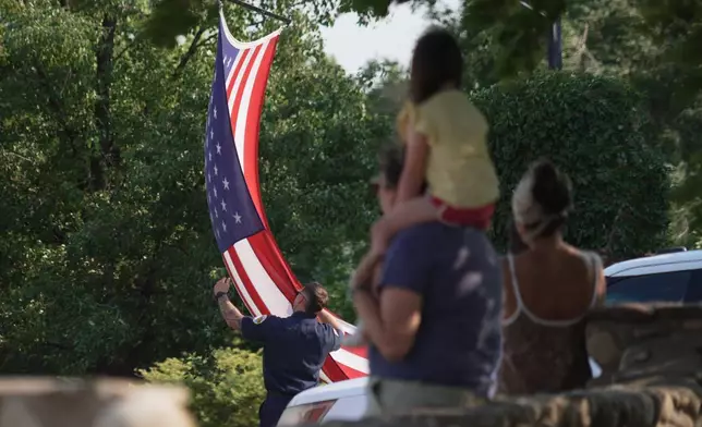A first responder adjusts an American flag during a procession in Grand Junction, Colo., Monday, June 29, 2026, for firefighters who died battling blazes near the Colorado-Utah border. (AP Photo/Ty ONeil)