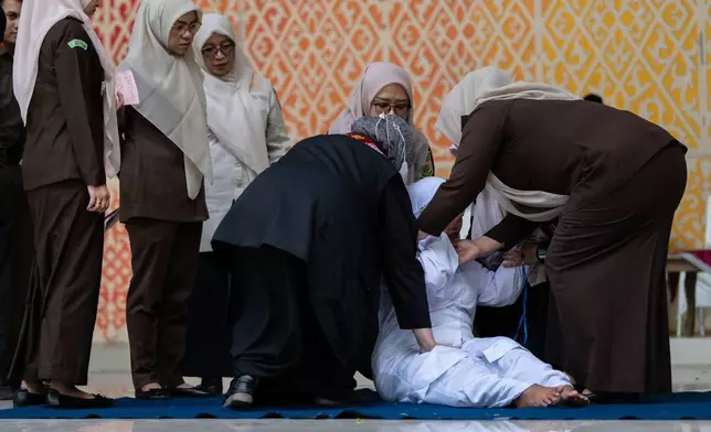 Shariah law officials assist an unmarried woman, convicted of violating Islamic law by kissing during a TikTok livestream, to get up after being being publicly caned, in Banda Aceh, Indonesia, Thursday, July 2, 2026. (AP Photo/Reza Saifullah)