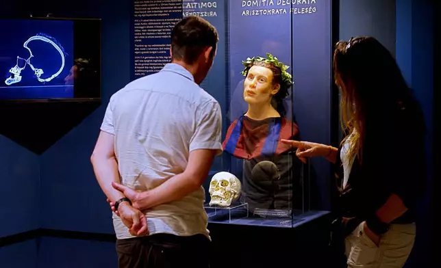 Visitors look at Roman-era skulls and their facial reconstructions in the Aquincum Museum's exhibition titled "Once we were like you" which showcases characters and the fictional life stories of those who once lived in the bustling Roman settlement of Aquincum, in Budapest, Hungary, Tuesday, July 7, 2026. (AP Photo/Bela Szandelszky)