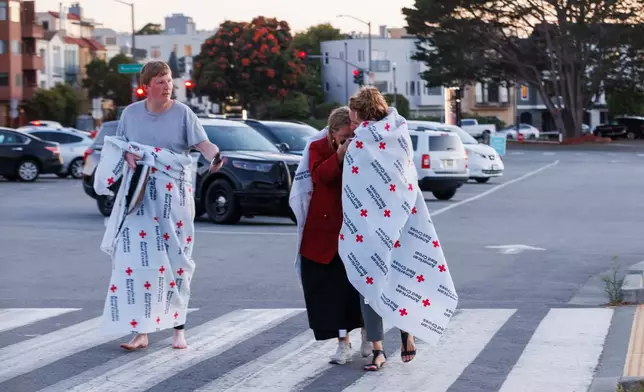 People cover themselves with American Red Cross blankets at Fort Mason, where the Red Cross has set up an assistance center for people impacted by a boat incident in the waters off San Francisco Tuesday, July 14, 2026. (Santiago Mejia/San Francisco Chronicle via AP)