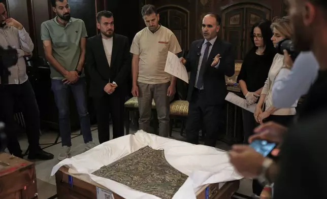 Ayman Nabou, deputy director-general of Antiquities and Museums, speaks as museum employees and officials gather around an antiquity returned from France at the National Museum in Damascus, Syria, Wednesday, July 8, 2026.(AP Photo/Ghaith Alsayed)