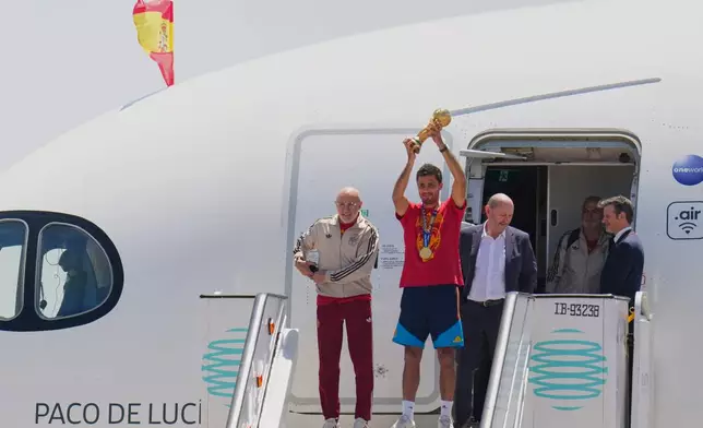 Spain's Rodrigo Hernandez lifts the World Cup trophy alongside Spain head coach Luis de la Fuente, left, and Royal Spanish Football Federation President Rafael Louzan as they arrive at Madrid airport on Monday, July 20, 2026, after Spain defeated Argentina in the World Cup final. (AP Photo/Manu Fernandez)