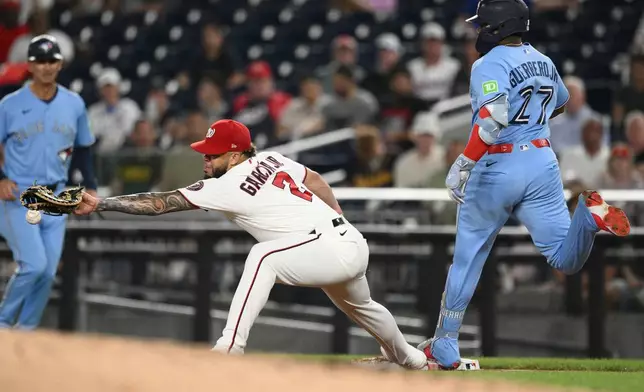 Toronto Blue Jays' Vladimir Guerrero Jr. (27) is safe at first base against Washington Nationals first baseman Luis Garcia Jr. (2) during the third inning of a baseball game, Tuesday, July 28, 2026, in Washington. (AP Photo/Nick Wass)