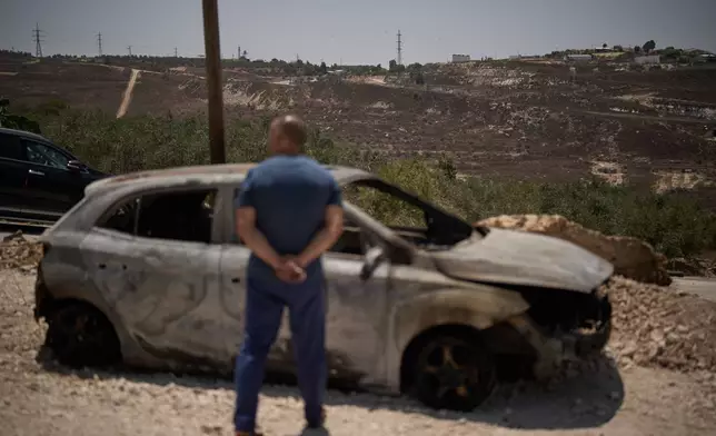 With the Israeli settlement of Khavat Gilad in the background, a Palestinian man stands in front of a burned car following an attack by Israeli settlers the previous day in the village of Sarra, near the West Bank city of Nablus, Saturday, July 25, 2026. (AP Photo/Leo Correa)