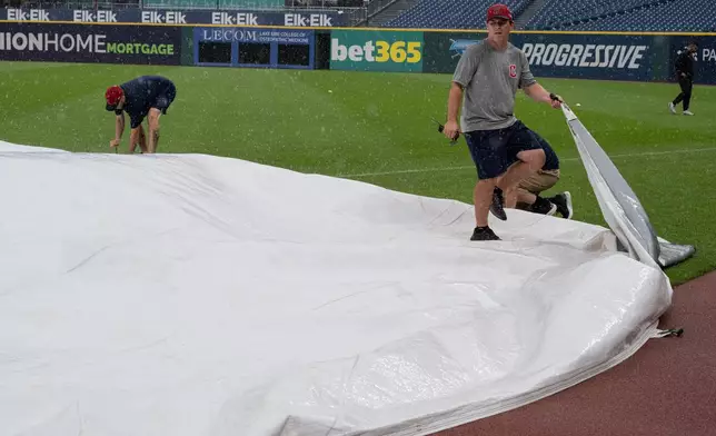 Progressive Field grounds crew apply the tarp during a rain shower before a baseball game between the Chicago White Sox and the Cleveland Guardians, Sunday, July 5, 2026, in Cleveland. (AP Photo/Phil Long)