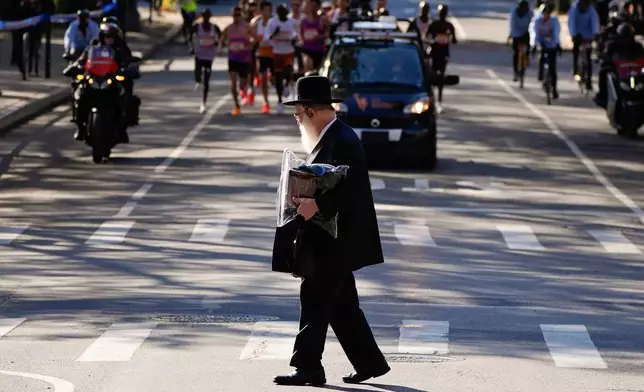 FILE - An Orthodox Jewish man crosses the street as athletes in the men's elite division make their way through Brooklyn during the New York City Marathon, Nov. 2, 2025, in New York. (AP Photo/Yuki Iwamura, File)