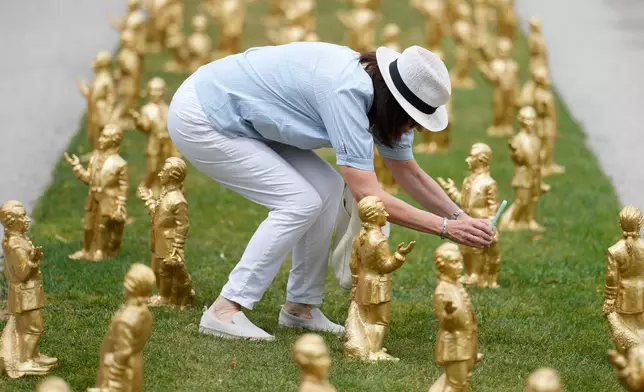 A woman takes pictures of 400 gold colored plastic Mozart sculptures by German artist Ottmar Hoerl from Nuremberg before the 270th birthday of composer Wolfgang Amadeus Mozart in Salzburg, Austria, Wednesday, July 15, 2026. (AP Photo/Matthias Schrader)
