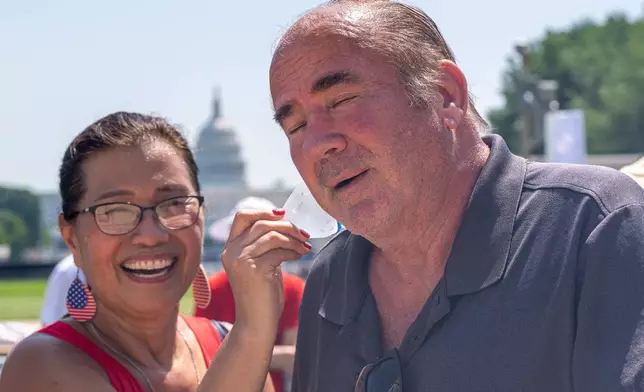 Stephanie McCallister holds a cold bottle of water to her husband Don McCallister's neck as they wait in line for the ferris wheel at the Great American State Fair on the National Mall, Wednesday, July 1, 2026, in Washington. (AP Photo/Jen Golbeck)